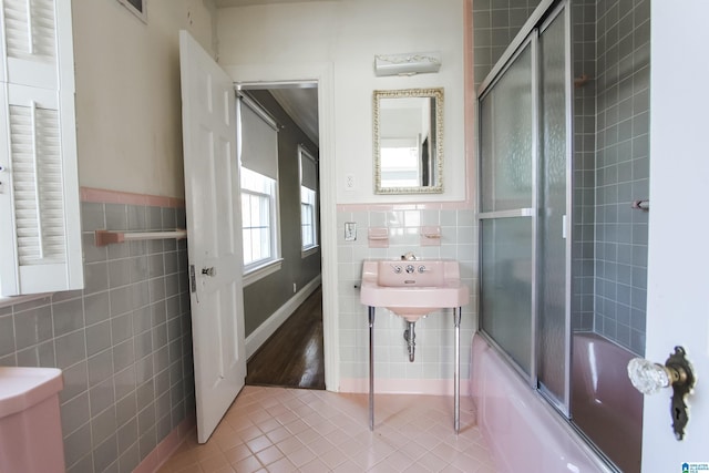 full bath with a wainscoted wall, tile walls, bath / shower combo with glass door, toilet, and tile patterned flooring