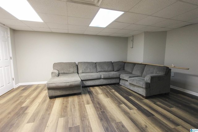 unfurnished living room with a paneled ceiling, baseboards, and wood finished floors