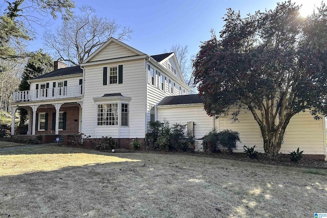 view of front of home featuring a porch, a chimney, a front yard, and a balcony