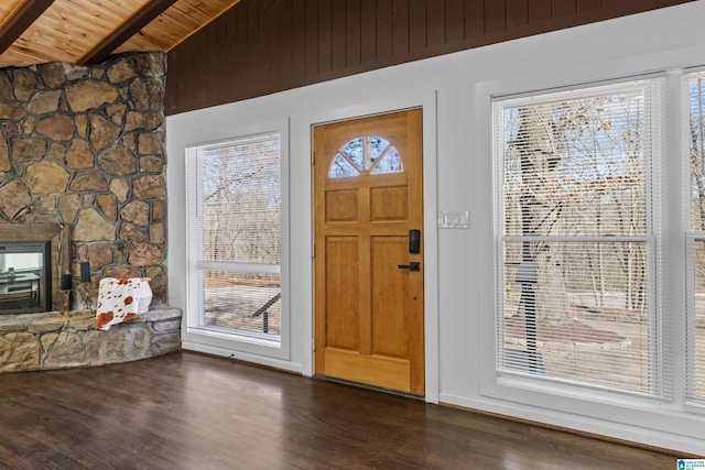 entryway with vaulted ceiling with beams, wood ceiling, dark wood-type flooring, and a stone fireplace