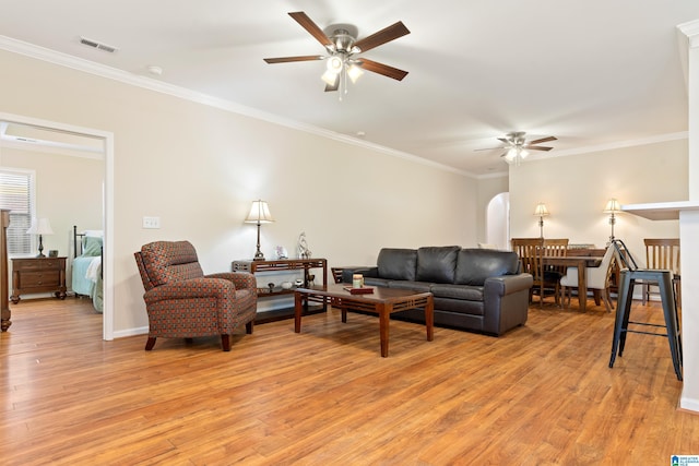 living room with light wood-style flooring, visible vents, arched walkways, and crown molding