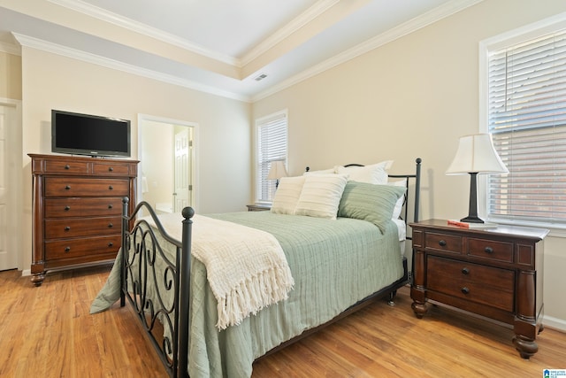 bedroom featuring visible vents, a raised ceiling, light wood finished floors, ensuite bath, and crown molding