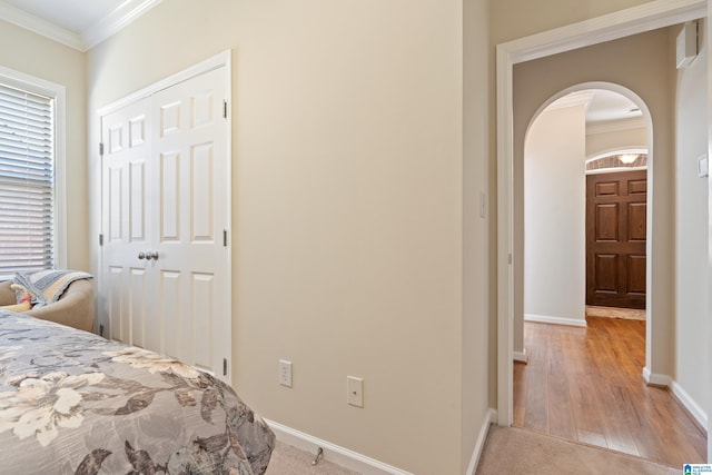 bedroom with light wood finished floors, baseboards, arched walkways, ornamental molding, and a closet