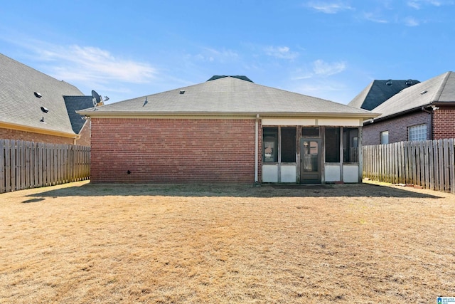 rear view of house with a sunroom, brick siding, a lawn, and a fenced backyard