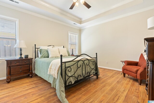 bedroom with light wood-type flooring, a tray ceiling, visible vents, and baseboards