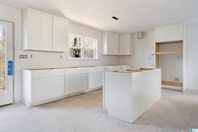 kitchen with concrete flooring, a kitchen island, and white cabinetry