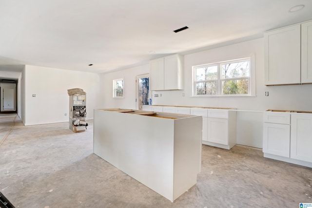 kitchen with concrete flooring, a kitchen island, white cabinetry, and a healthy amount of sunlight