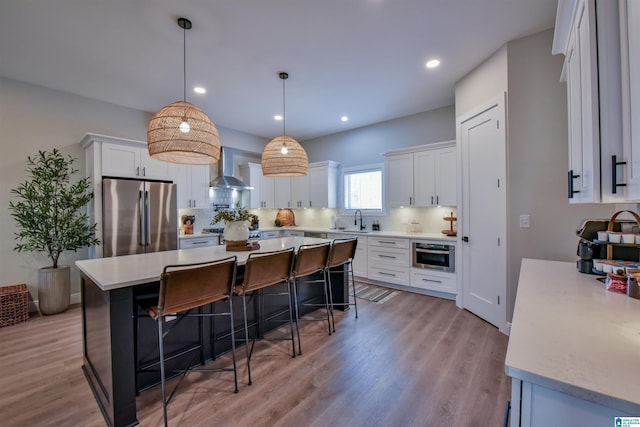 kitchen with light countertops, hanging light fixtures, freestanding refrigerator, white cabinetry, and wall chimney range hood