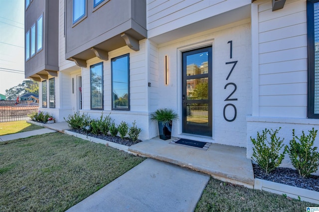 view of exterior entry with a lawn and brick siding