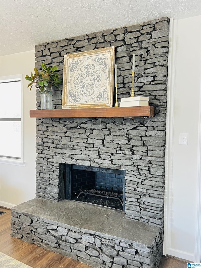 interior details with a textured ceiling, a stone fireplace, wood finished floors, and baseboards