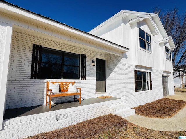 doorway to property featuring a garage, covered porch, board and batten siding, and brick siding