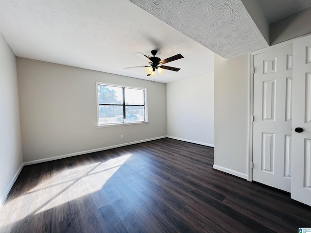 unfurnished room featuring a ceiling fan, a textured ceiling, baseboards, and dark wood-type flooring