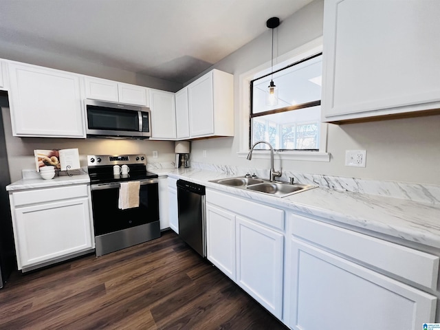 kitchen featuring dark wood finished floors, stainless steel appliances, hanging light fixtures, white cabinetry, and a sink