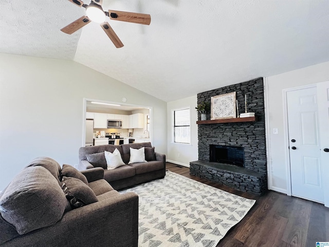 living room with dark wood-style flooring, lofted ceiling, ceiling fan, a stone fireplace, and a textured ceiling