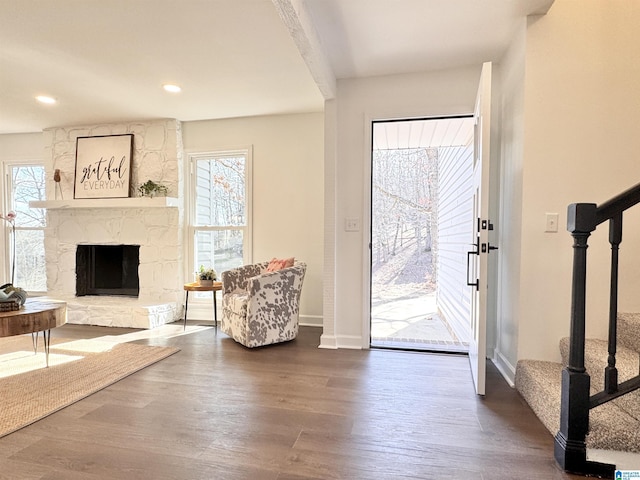 interior space with baseboards, wood finished floors, stairs, a stone fireplace, and recessed lighting