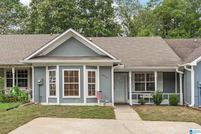 view of front of home with covered porch, a front yard, and roof with shingles