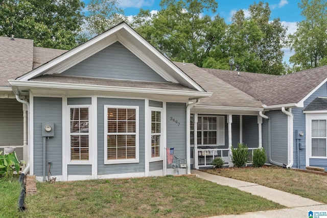 view of front of property featuring a porch, a shingled roof, and a front yard