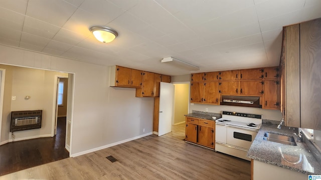 kitchen with brown cabinetry, wood finished floors, heating unit, range hood, and double oven range