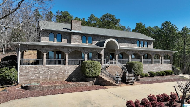 view of front facade with stairs, a chimney, a porch, and brick siding