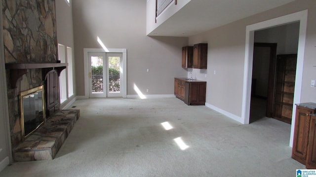 unfurnished living room featuring light carpet, a fireplace, baseboards, and a high ceiling