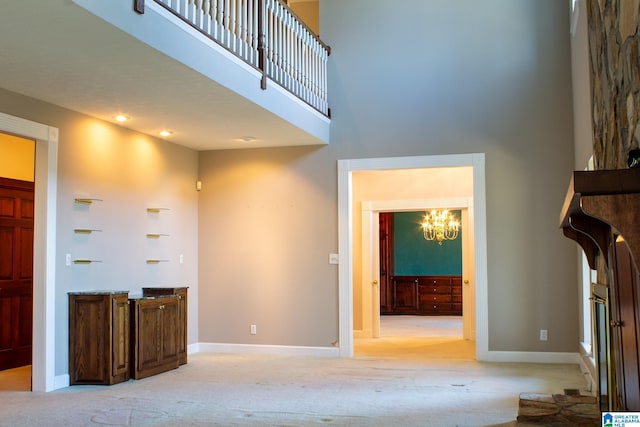 unfurnished living room with light carpet, an inviting chandelier, a high ceiling, and baseboards