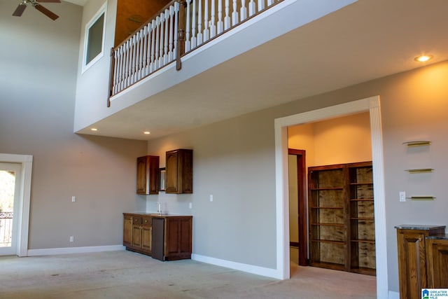 unfurnished living room with light carpet, a towering ceiling, baseboards, and a sink