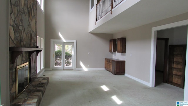 unfurnished living room with a fireplace, a towering ceiling, light carpet, a sink, and baseboards