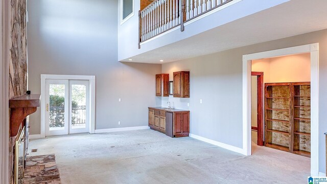 unfurnished living room with baseboards, a high ceiling, a sink, and light colored carpet