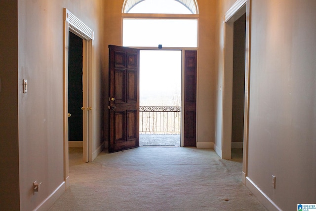 hallway with light carpet, a towering ceiling, and baseboards