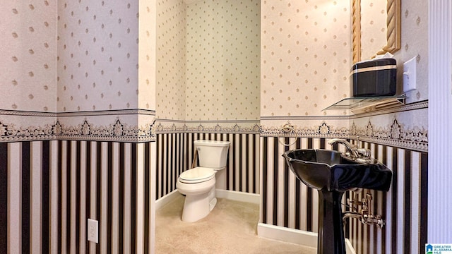 bathroom with toilet, wallpapered walls, and baseboards