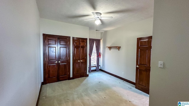 unfurnished bedroom with light carpet, ceiling fan, baseboards, and a textured ceiling