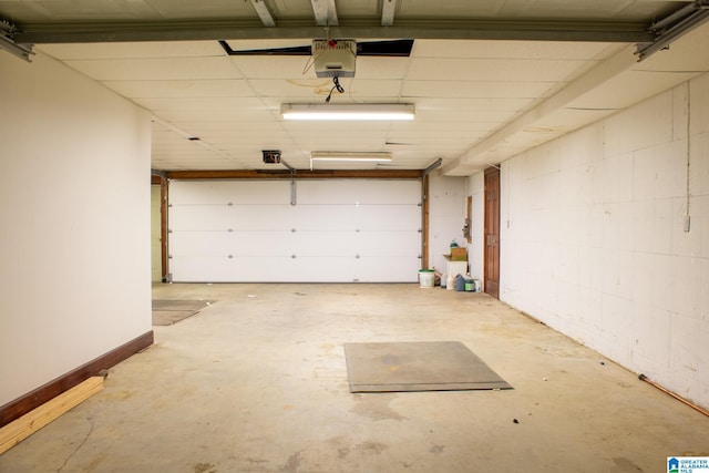 garage with concrete block wall, baseboards, and a garage door opener