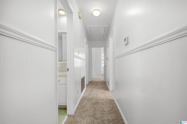 hallway featuring a wainscoted wall, attic access, and light colored carpet