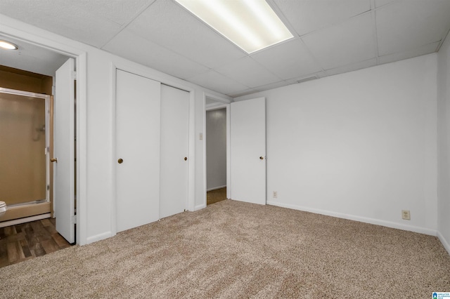 unfurnished bedroom with baseboards, connected bathroom, a drop ceiling, carpet flooring, and a closet