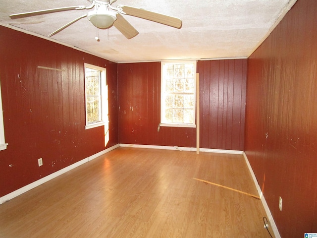 empty room with a textured ceiling, wooden walls, wood finished floors, a ceiling fan, and baseboards