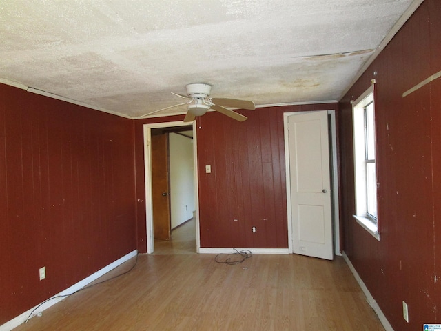 spare room featuring light wood finished floors, wooden walls, and a textured ceiling