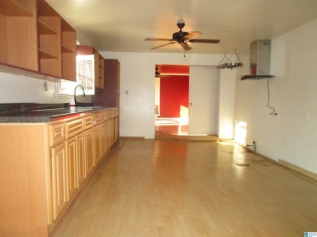 kitchen featuring dark countertops, light wood-type flooring, wall chimney range hood, open shelves, and a sink