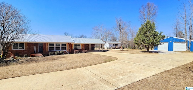 single story home with driveway, brick siding, metal roof, and an outbuilding