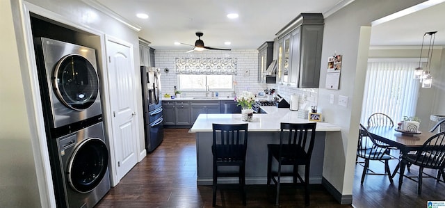 kitchen with a breakfast bar, pendant lighting, stacked washer / drying machine, light countertops, and a peninsula