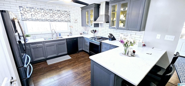 kitchen with a peninsula, a sink, appliances with stainless steel finishes, wall chimney exhaust hood, and glass insert cabinets