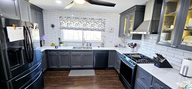 kitchen featuring glass insert cabinets, wall chimney range hood, light countertops, black appliances, and a sink