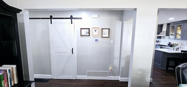 interior space with a barn door, visible vents, baseboards, wall chimney range hood, and decorative backsplash