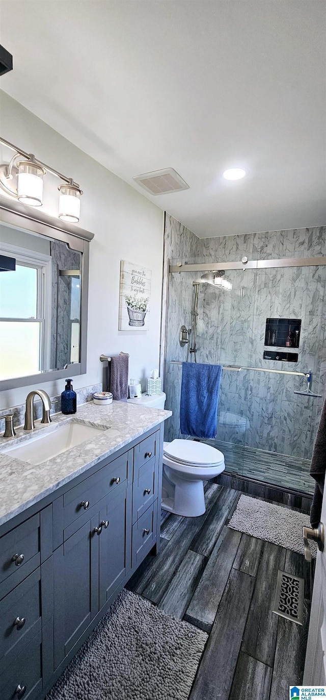 bathroom featuring toilet, wood finished floors, visible vents, vanity, and a stall shower