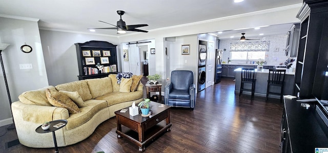 living area featuring a ceiling fan, dark wood-style flooring, stacked washing maching and dryer, and a barn door