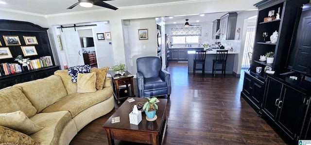 living area featuring dark wood-type flooring, ceiling fan, ornamental molding, and a barn door