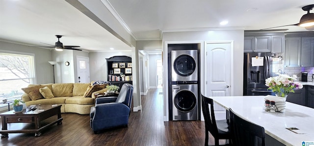 living room featuring ceiling fan, ornamental molding, dark wood-style flooring, and stacked washer / drying machine