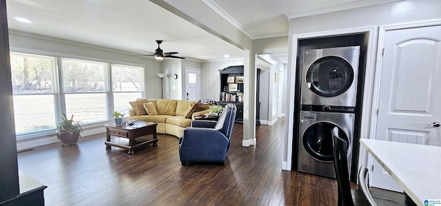 living area with baseboards, stacked washing maching and dryer, dark wood finished floors, and crown molding