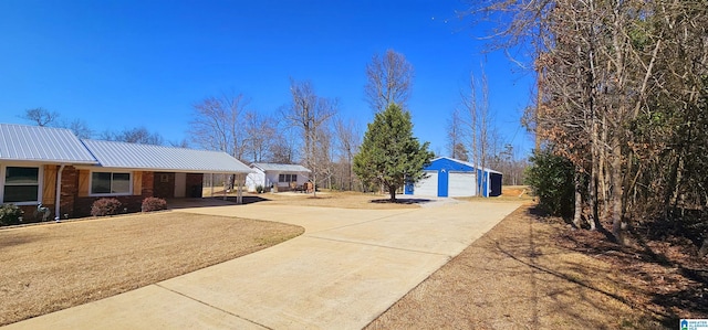 single story home featuring an outbuilding, metal roof, brick siding, concrete driveway, and a front lawn