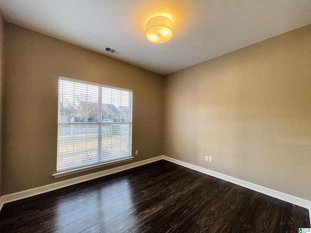 spare room with dark wood-style floors, visible vents, and baseboards