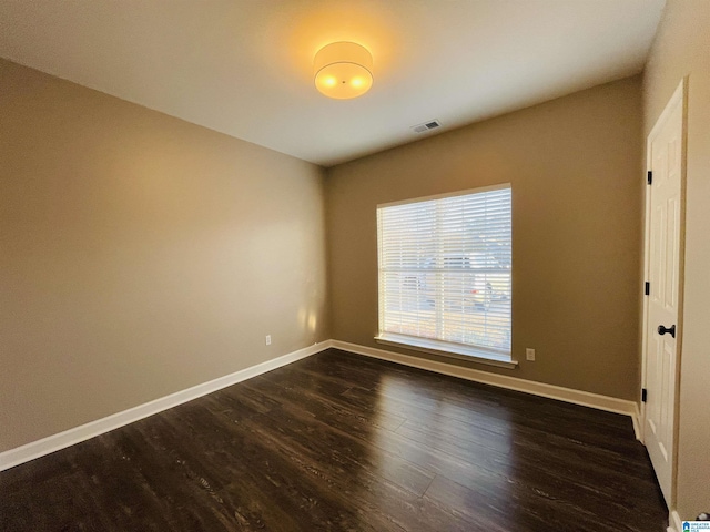 empty room featuring visible vents, baseboards, and dark wood-type flooring